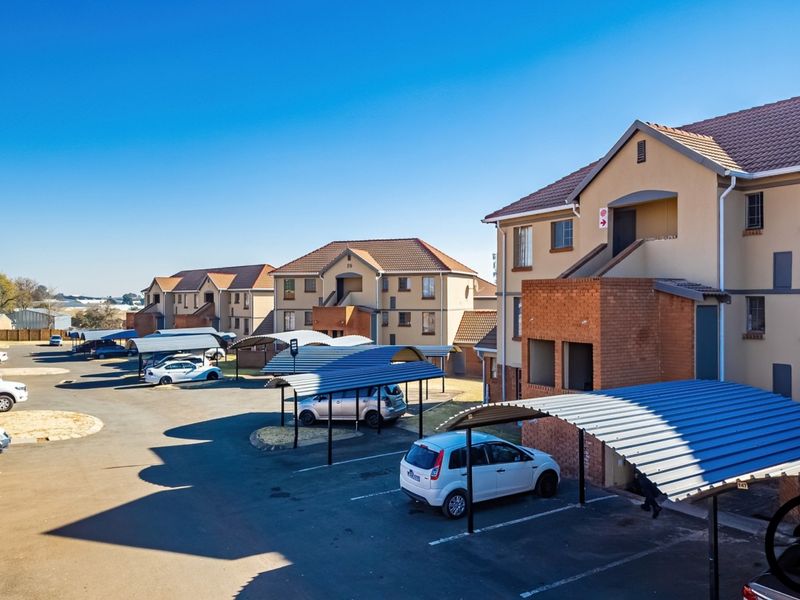 Exterior view of a multi-story apartment complex featuring brick and plaster facades, tiled roofing, and dedicated covered parking bays for residents.