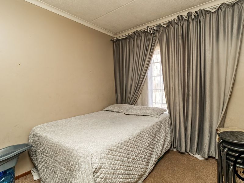 A compact bedroom featuring carpeted flooring and a window with full-length curtains, offering a functional space that could benefit from cosmetic updates.