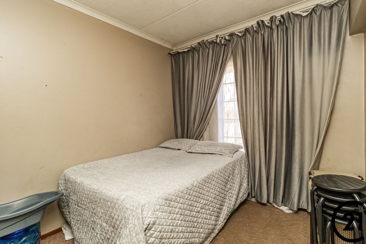 A compact bedroom featuring carpeted flooring and a window with full-length curtains, offering a functional space that could benefit from cosmetic updates.