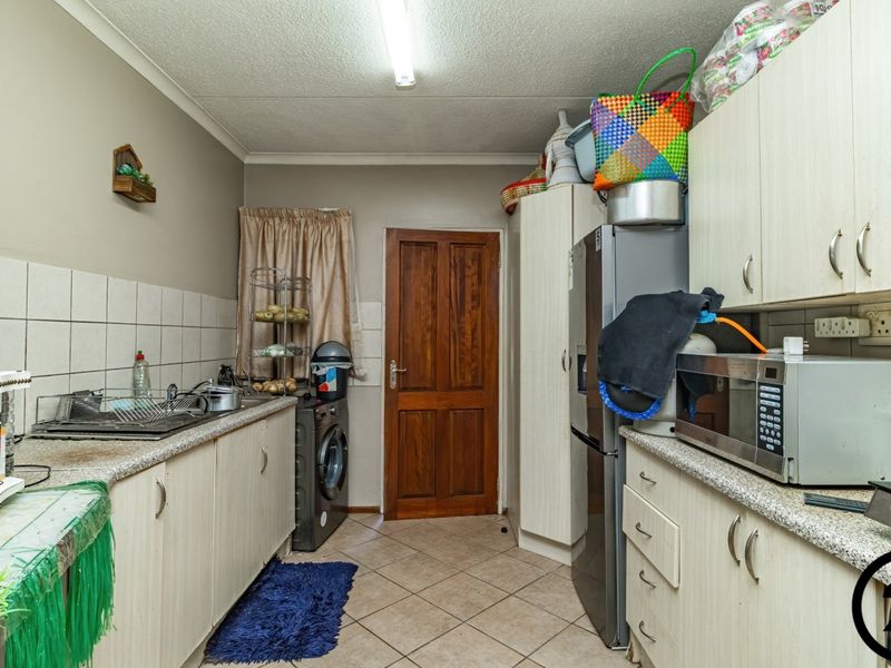 A functional kitchen featuring laminate cabinetry, tiled backsplash, and ceramic flooring, offering a practical layout with integrated space for laundry appliances.