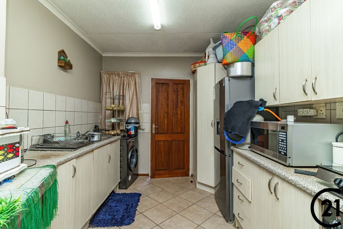 A functional kitchen featuring laminate cabinetry, tiled backsplash, and ceramic flooring, offering a practical layout with integrated space for laundry appliances.