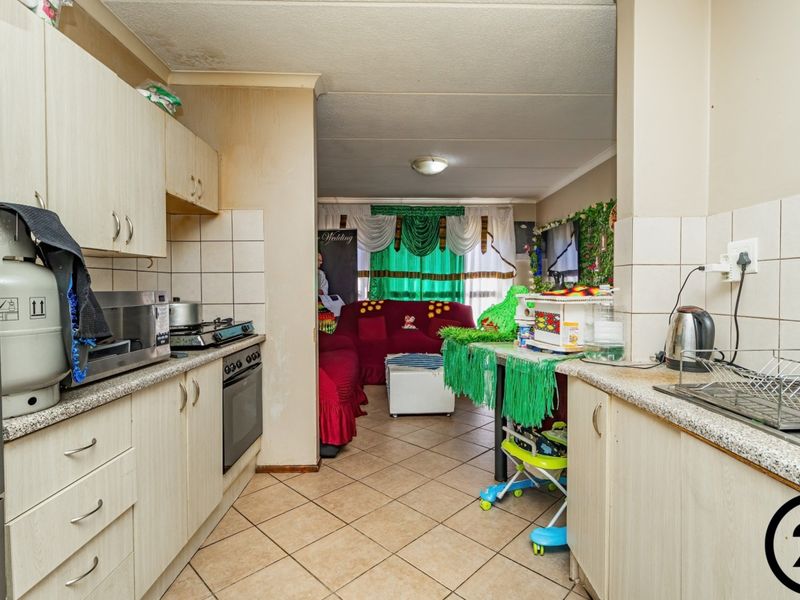 Open-plan kitchen and living area featuring tiled flooring, built-in cabinetry, and a gas hob, requiring cosmetic updates to improve the overall aesthetic.
