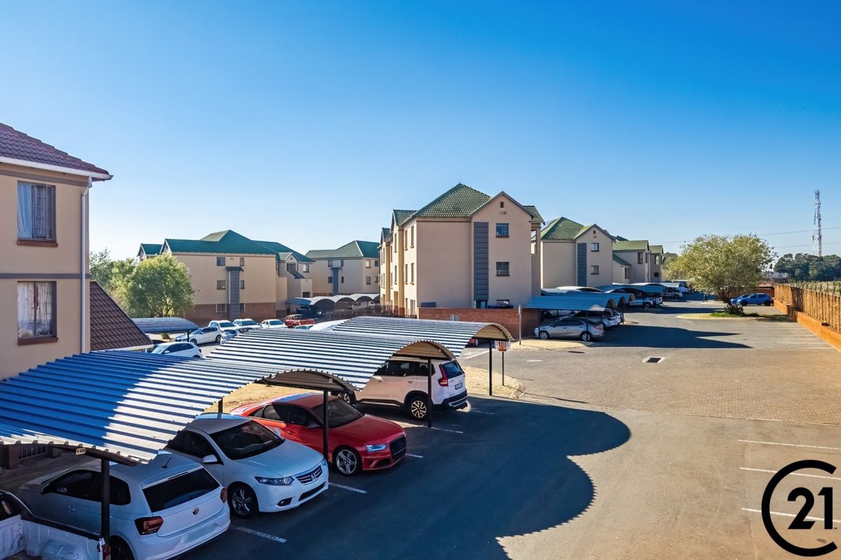An elevated view of an apartment complex featuring multiple residential buildings, paved parking areas, and covered carports for residents.