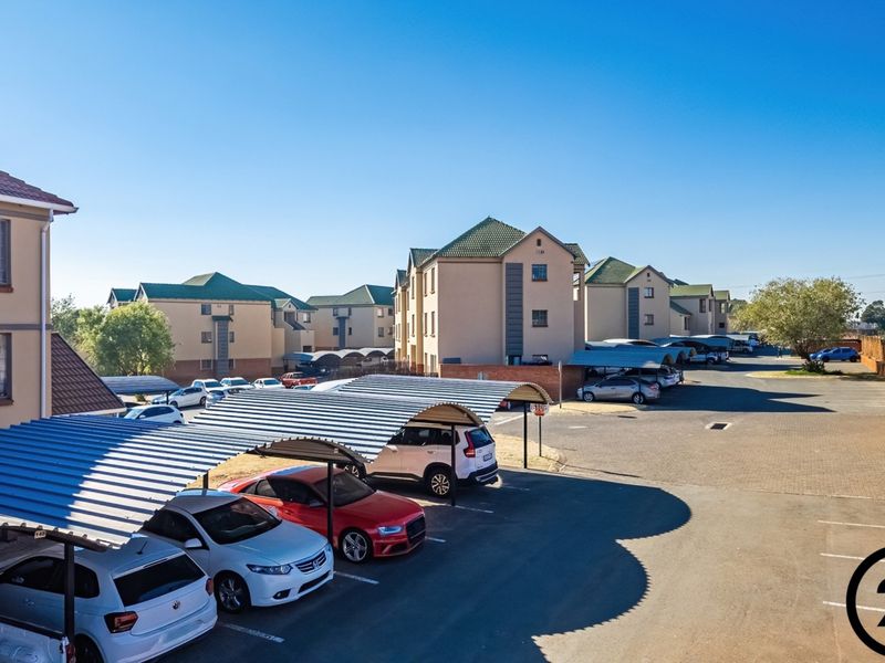An elevated view of an apartment complex featuring multiple residential buildings, paved parking areas, and covered carports for residents.