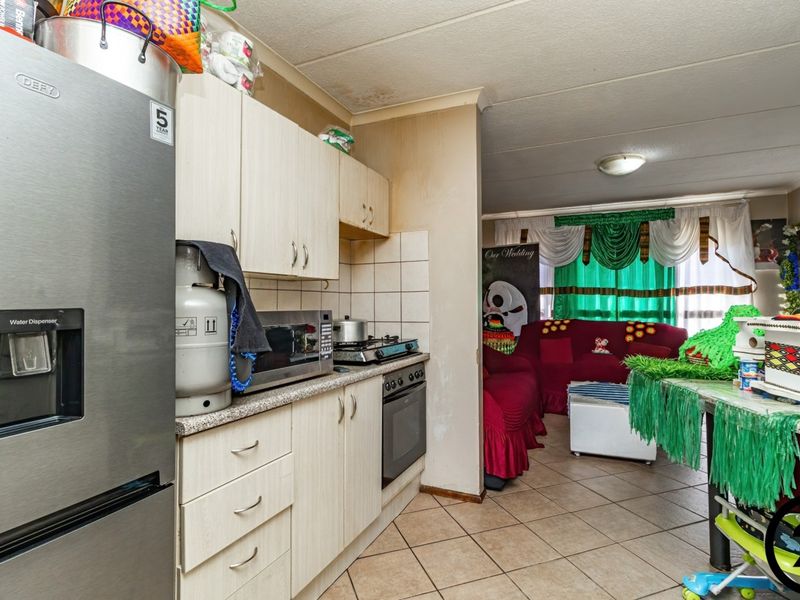 Open-plan kitchen and living area featuring tiled flooring, built-in cabinetry, and a gas hob, showing signs of wear and ceiling water damage.