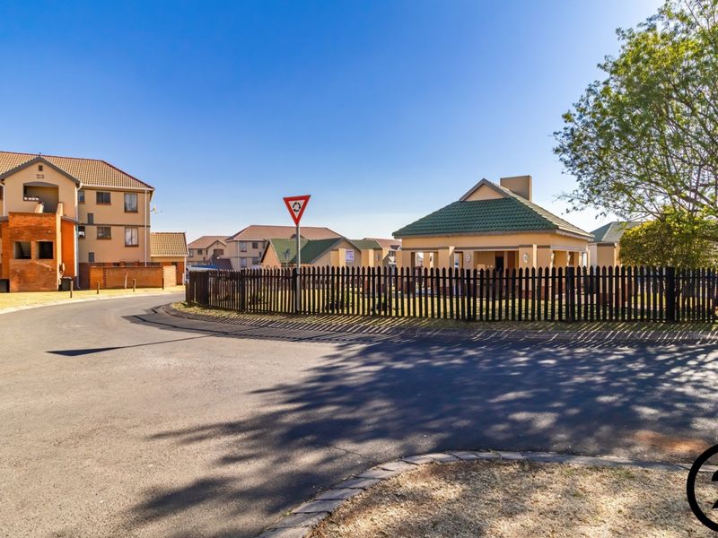 A street view of a residential apartment complex featuring paved roads, perimeter fencing, and multiple buildings with tiled roofs.