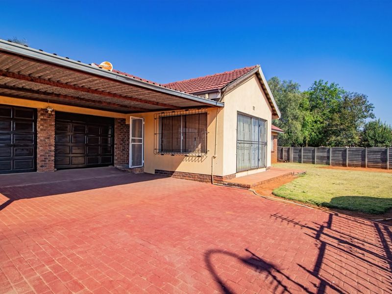 Front exterior view featuring a brick paved driveway, covered carport, double garage, and security bars on windows.