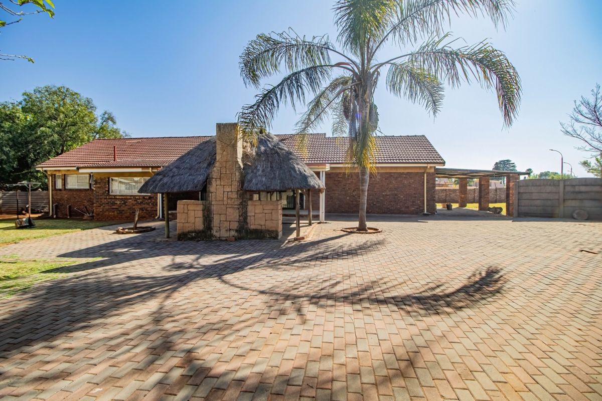 Spacious rear exterior featuring a paved courtyard, a traditional thatched lapa with a built-in brick fireplace, and established garden surroundings.