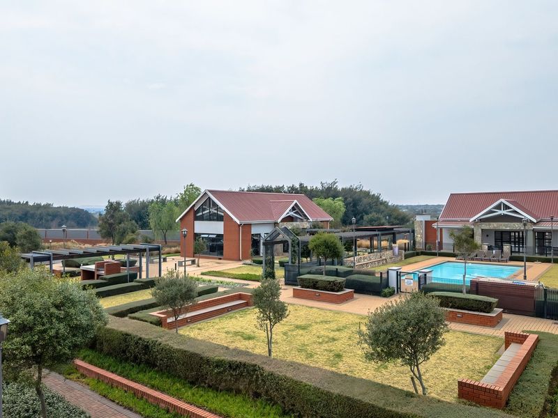 Elevated view of a well-maintained apartment complex communal area featuring a swimming pool, landscaped gardens, brick pathways, and outdoor entertainment structures.