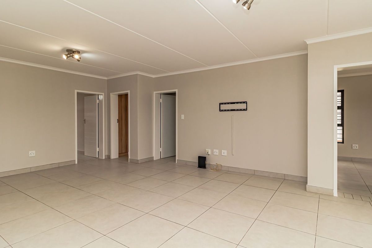 A spacious, empty living area featuring neutral tiled flooring, clean painted walls, and multiple internal doorways leading to other parts of the apartment.