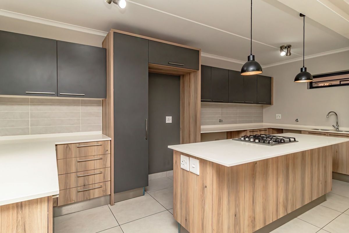 Modern kitchen featuring two-tone cabinetry, stone countertops, a central island with a gas hob, and high-quality finishes throughout.