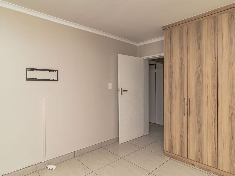 A clean, neutral bedroom featuring light-toned tiled flooring and a large, modern built-in wardrobe with wood-grain finish.