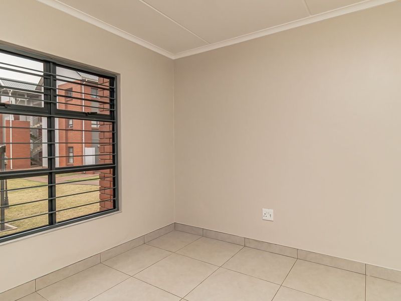 A clean, empty bedroom featuring neutral tiled flooring, smooth walls, and a window fitted with security bars.
