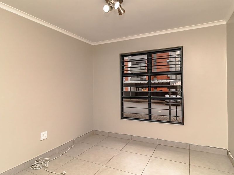 A clean, empty bedroom featuring neutral wall paint, tiled flooring, and a window fitted with security bars.