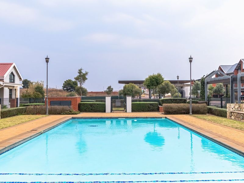 A well-maintained communal swimming pool area featuring stone-clad seating, paved surrounds, and pergola structures within a residential apartment complex.