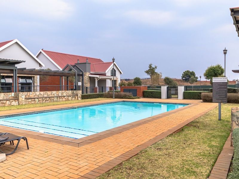 A well-maintained communal swimming pool area featuring brick paving, stone-clad retaining walls, and a pergola structure within a residential complex.