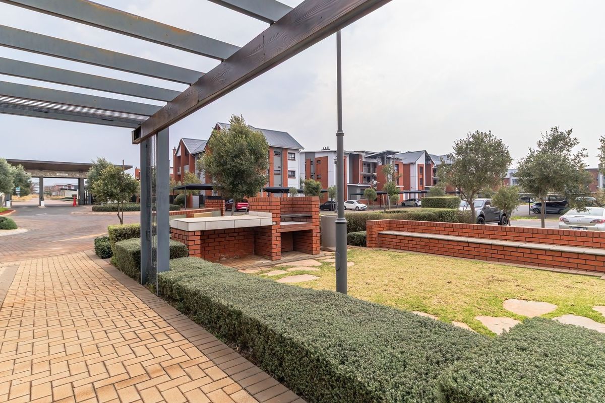 Communal outdoor area featuring a brick built-in braai, brick bench seating, and a pergola, set within a well-maintained residential apartment complex.