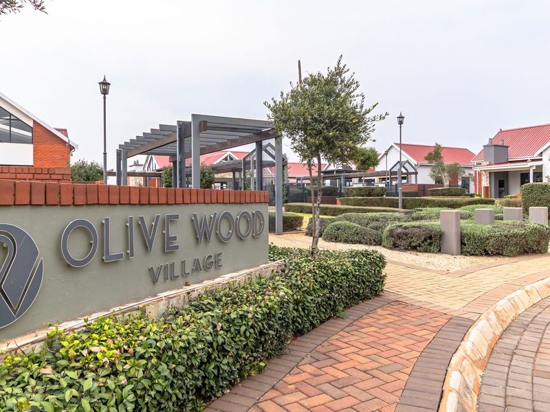 Entrance view of Olive Wood Village featuring well-maintained brick paving, landscaped gardens, and modern signage.