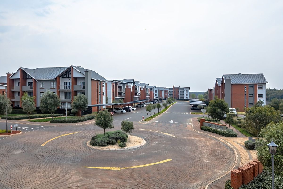 An elevated aerial view of a modern residential apartment complex featuring brick buildings, paved driveways, a central roundabout, and covered parking facilities.