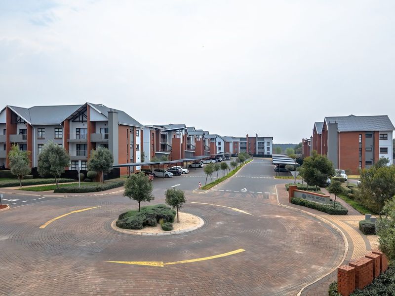An elevated aerial view of a modern residential apartment complex featuring brick buildings, paved driveways, a central roundabout, and covered parking facilities.