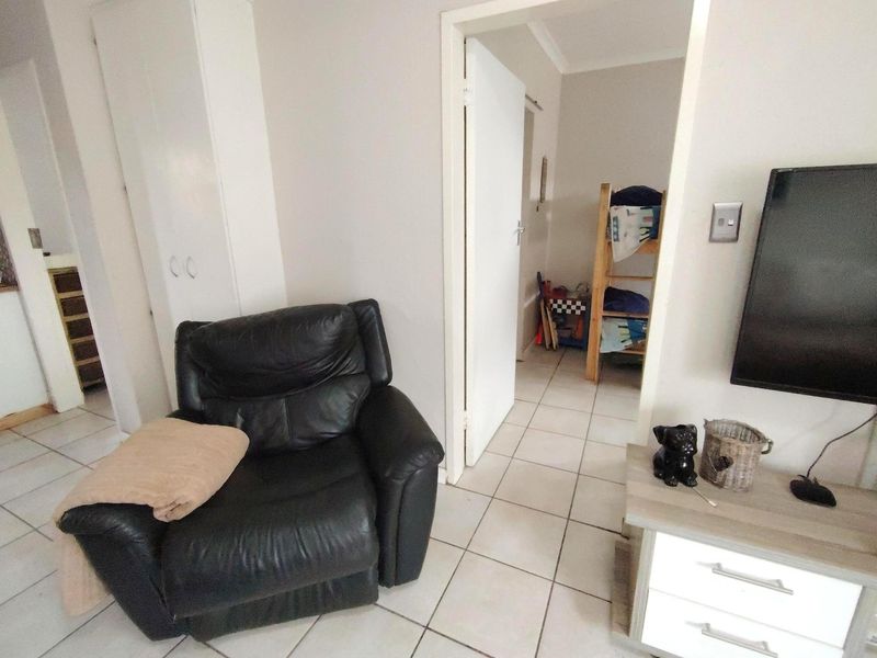 A living area featuring ceramic floor tiles and a built-in cupboard, with a doorway leading to an adjacent bedroom.