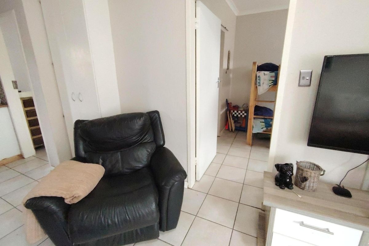 A living area featuring ceramic floor tiles and a built-in cupboard, with a doorway leading to an adjacent bedroom.