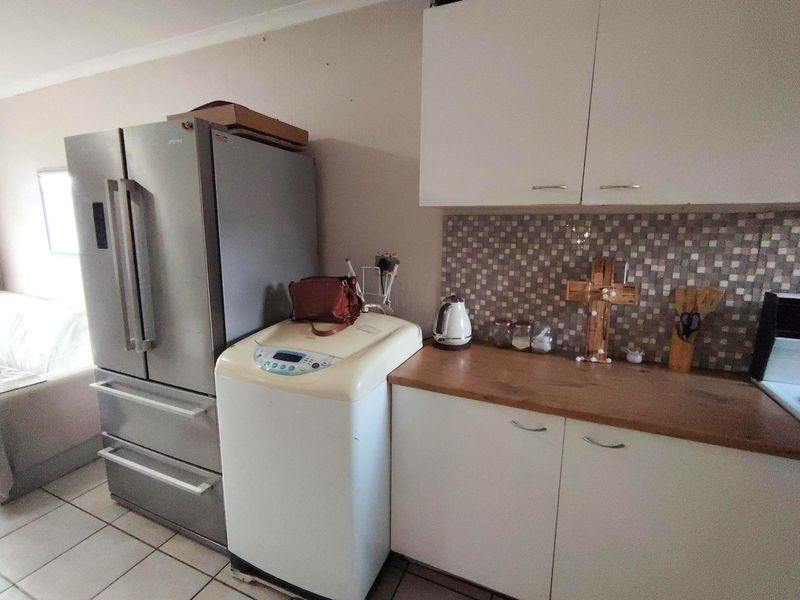 A functional kitchen area featuring white cabinetry, a mosaic tile backsplash, wooden countertops, and tiled flooring.