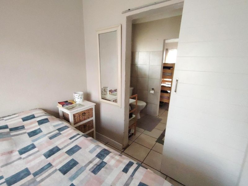 A bedroom featuring tiled flooring and a sliding door leading to an en-suite bathroom with wall tiles and a toilet.