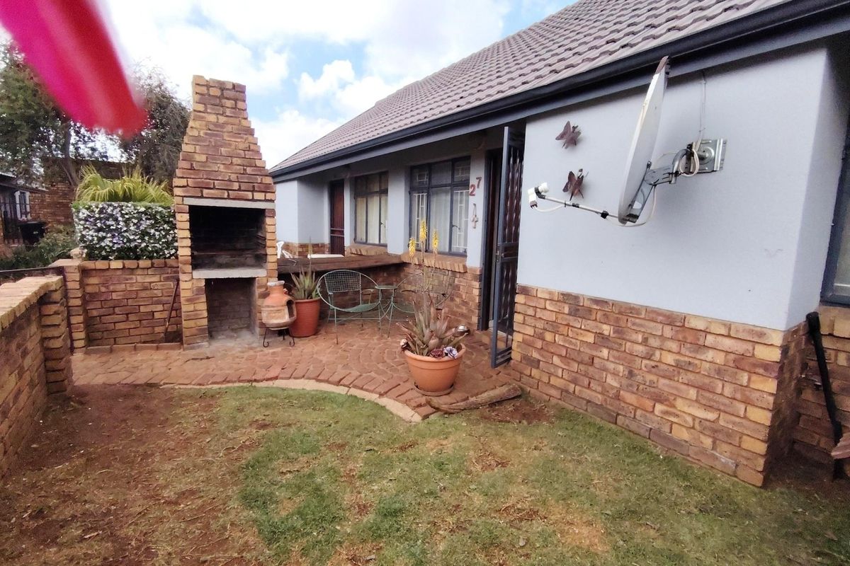 Rear exterior view of the townhouse featuring a built-in brick braai, paved patio area, and small garden space.