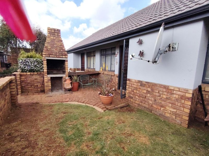Rear exterior view of the townhouse featuring a built-in brick braai, paved patio area, and small garden space.