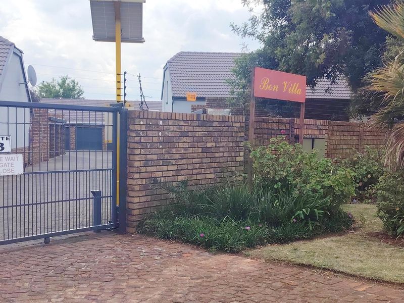 Front entrance view of the Bon Villa townhouse complex, featuring a brick boundary wall, secure sliding gate, and solar-powered lighting infrastructure.