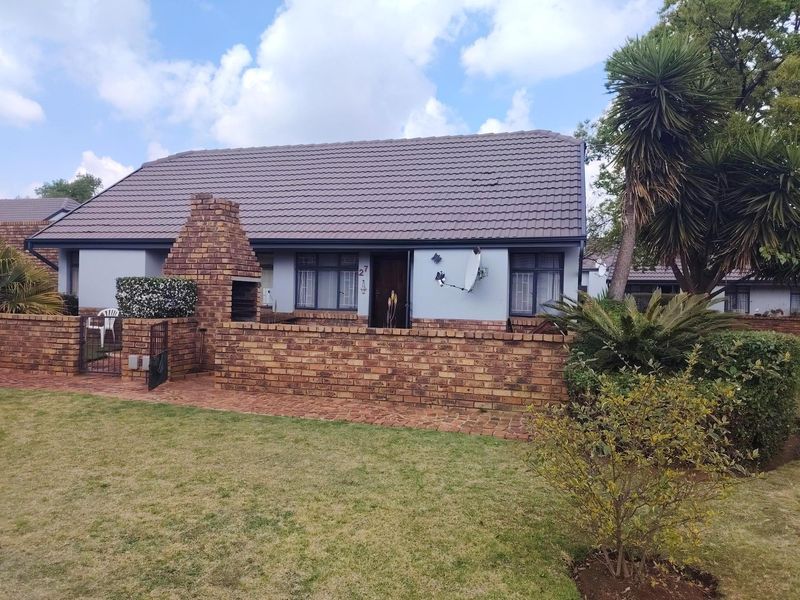 Front exterior view of a townhouse featuring a brick facade, tiled roof, and a built-in brick braai area with a small garden.