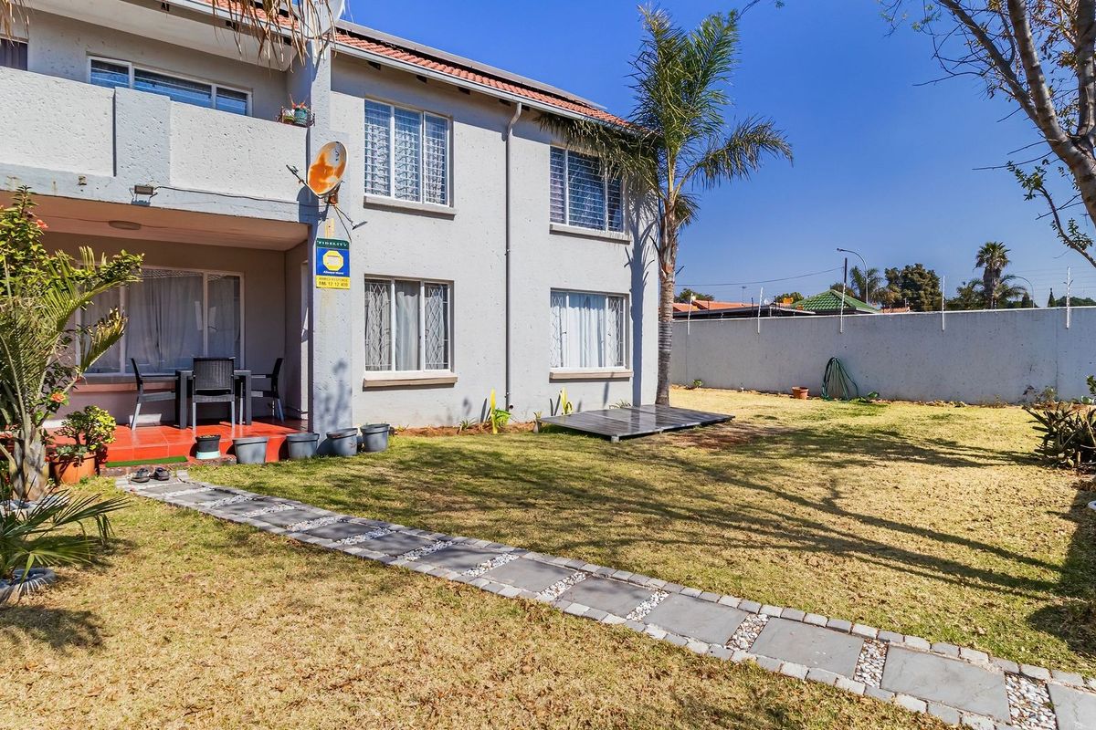 Rear view of the apartment building featuring a private garden, paved walkway, and a covered patio area.