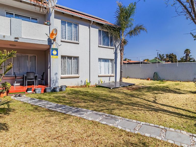 Rear view of the apartment building featuring a private garden, paved walkway, and a covered patio area.