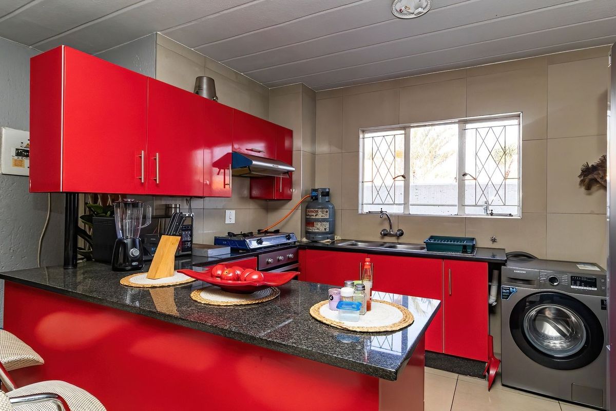 A functional kitchen featuring vibrant red cabinetry, granite countertops, a gas stove, and integrated laundry plumbing, finished with neutral wall tiling.