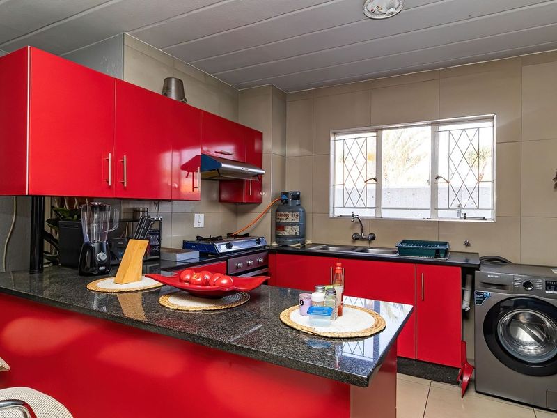 A functional kitchen featuring vibrant red cabinetry, granite countertops, a gas stove, and integrated laundry plumbing, finished with neutral wall tiling.
