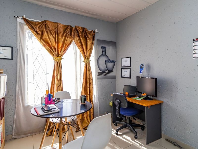 A functional bedroom space featuring tiled flooring and a window fitted with security bars, currently utilized as a home office and study area.