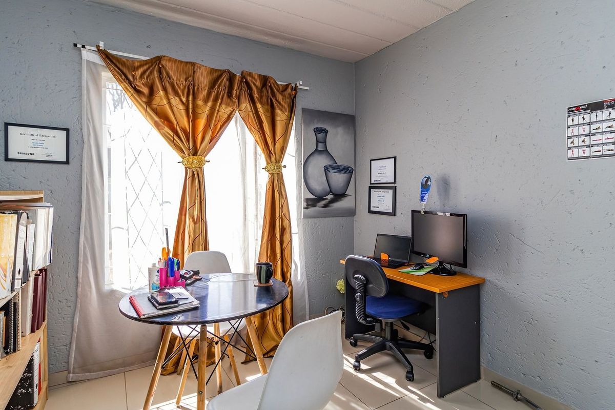 A functional bedroom space featuring tiled flooring and a window fitted with security bars, currently utilized as a home office and study area.