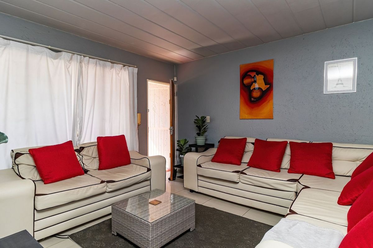 A living room featuring tiled flooring, textured grey walls, and a panelled ceiling, providing a functional and comfortable lounge space.