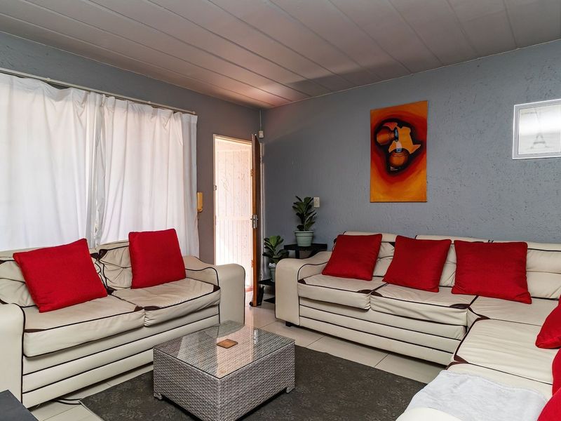 A living room featuring tiled flooring, textured grey walls, and a panelled ceiling, providing a functional and comfortable lounge space.