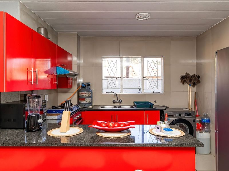 A functional kitchen featuring vibrant red cabinetry, granite countertops, a double basin sink, and a gas stove with an integrated extractor fan.