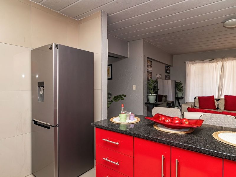 Open plan kitchen and living area featuring a granite countertop, red cabinetry, and tiled splashback, creating a functional and connected living space.