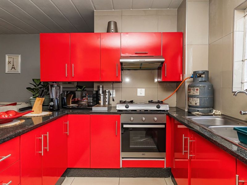 A functional kitchen featuring vibrant red cabinetry, granite countertops, a built-in gas hob, oven, extractor fan, and a double sink with tiled backsplash.