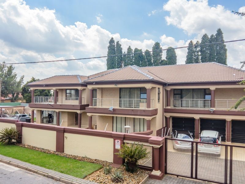 A multi-level residential property featuring a tiled roof, multiple balconies with steel railings, integrated garages, and a secure perimeter wall with electric fencing.