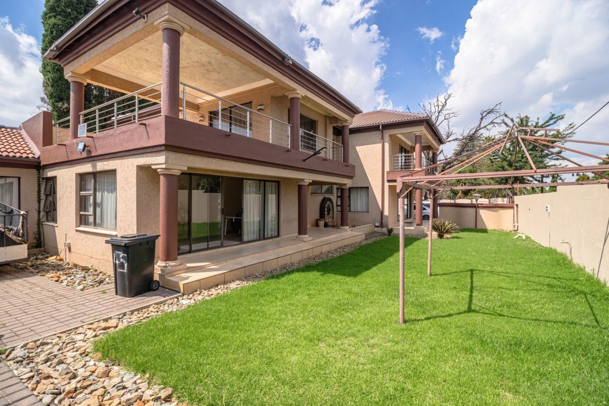 Rear view of a two-story house featuring a covered patio, upper-level balcony with metal railings, and a spacious garden area.