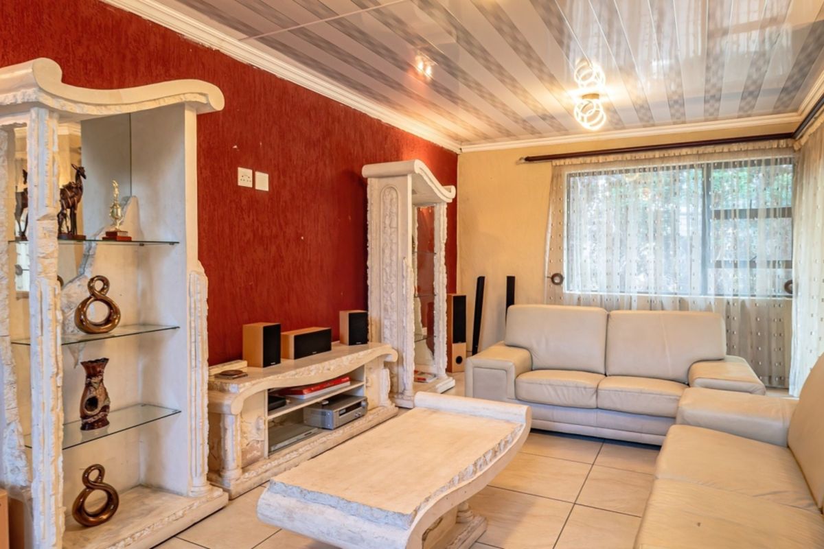 A living room featuring tiled flooring, textured red accent walls, and a coved ceiling with integrated display shelving.