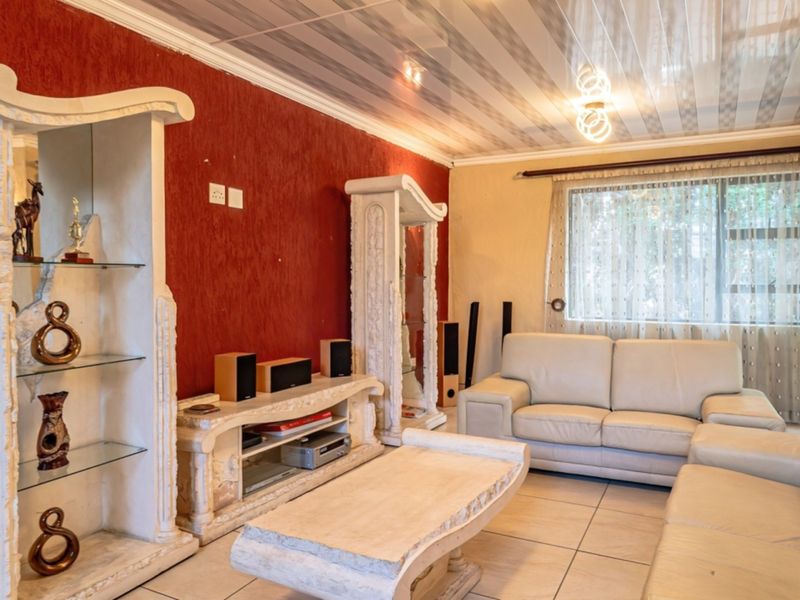 A living room featuring tiled flooring, textured red accent walls, and a coved ceiling with integrated display shelving.