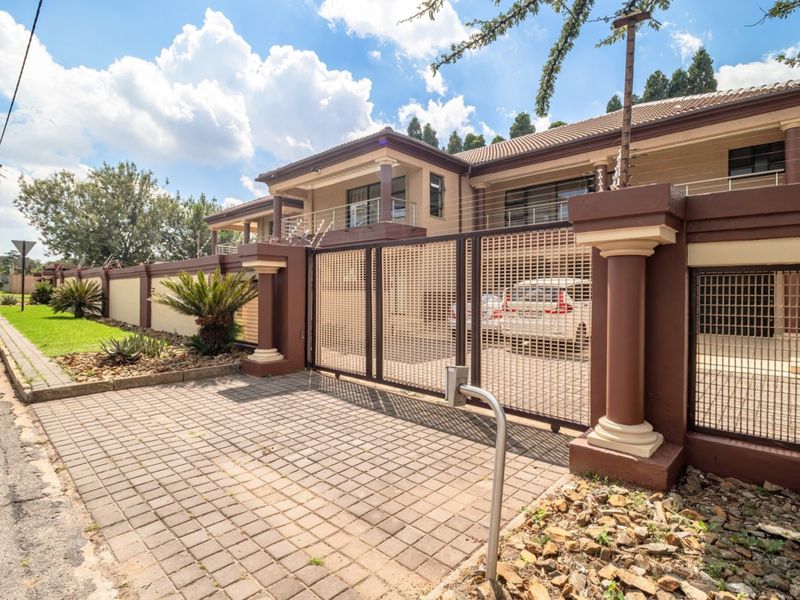 Front elevation of a multi-story residence featuring a paved driveway, secure electric gate, perimeter wall with electric fencing, and a balcony.