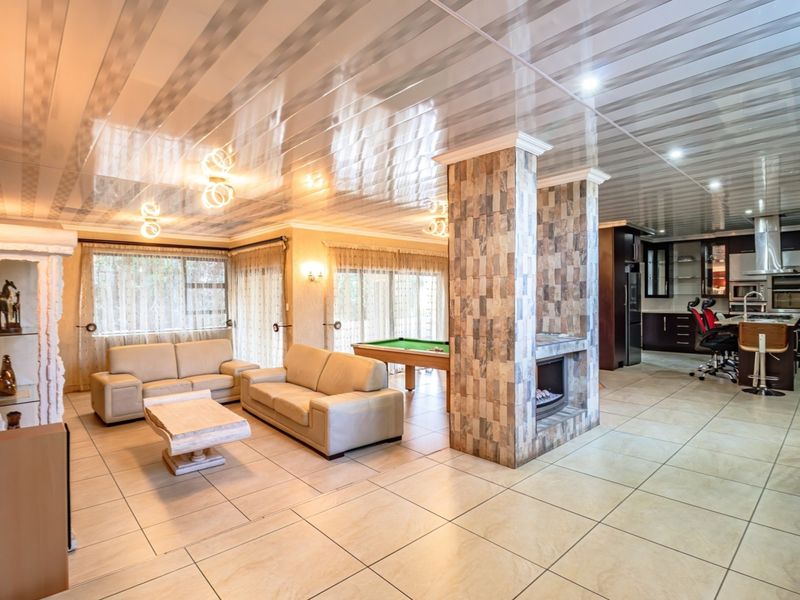 Spacious open-plan living and kitchen area featuring a central stone-clad fireplace, glossy ceiling panels, and large ceramic floor tiles throughout.