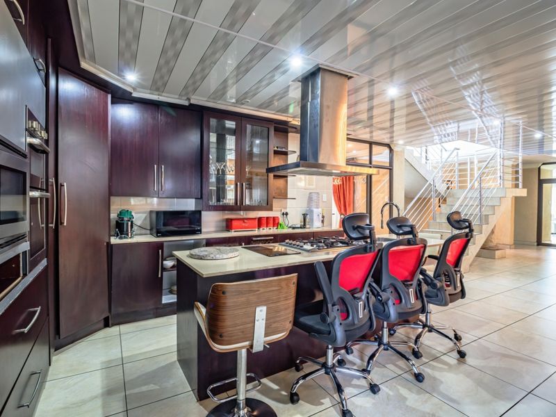 Modern kitchen featuring dark wood cabinetry, a central island with a gas hob, integrated appliances, and tiled flooring, adjacent to an open staircase.